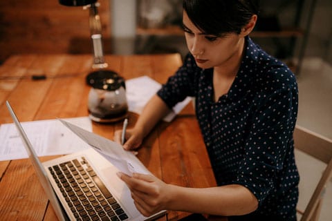 Woman reviewing a document while sitting in front of a laptop.